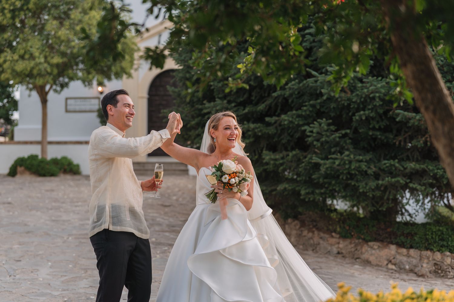 A couple celebrates with joy on stone courtyard outside a Mediterranean church.