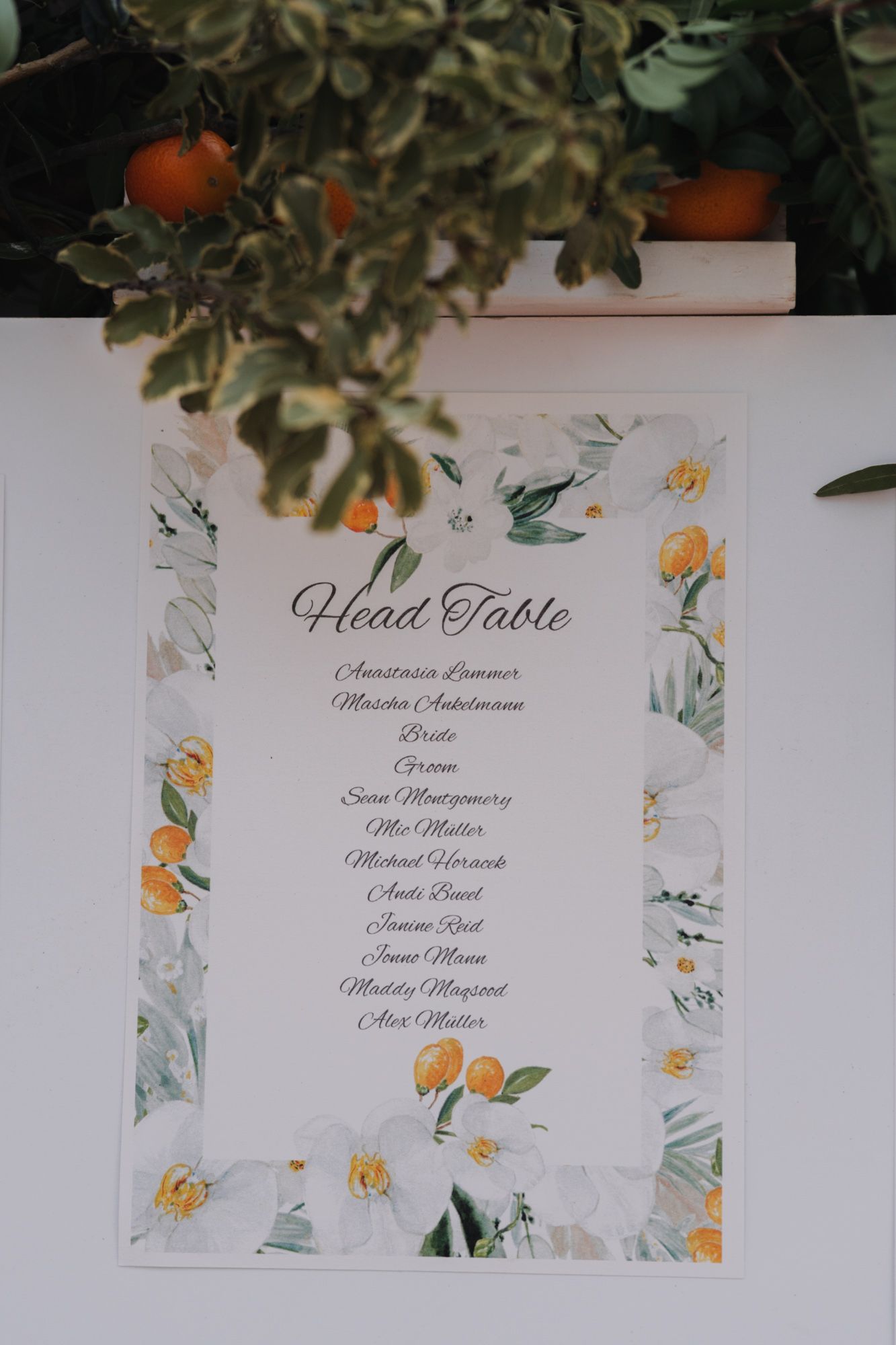 Wedding head table seating chart with orange and floral watercolor design under citrus branches.