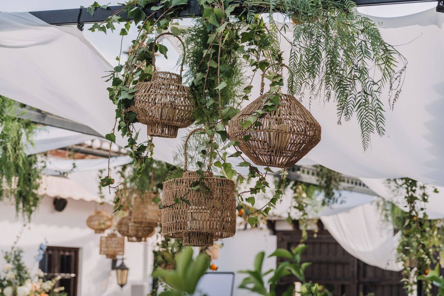 Rustic woven basket lanterns hanging with cascading greenery and white fabric draping.
