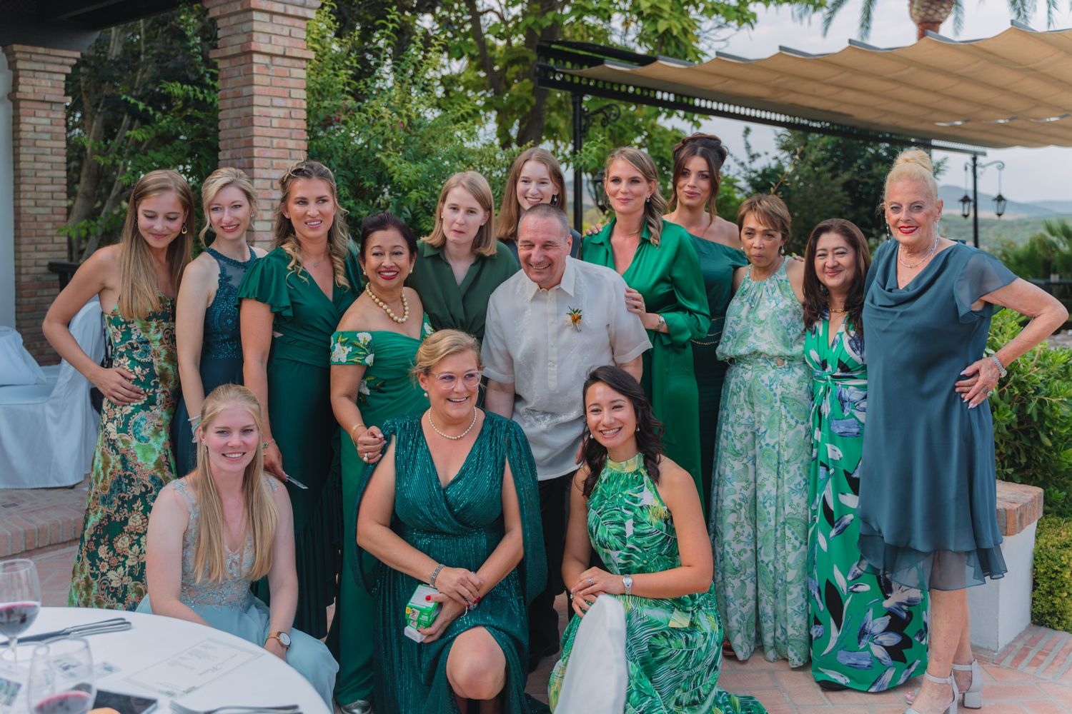 Wedding party group poses outdoors wearing coordinating emerald green and floral dresses.