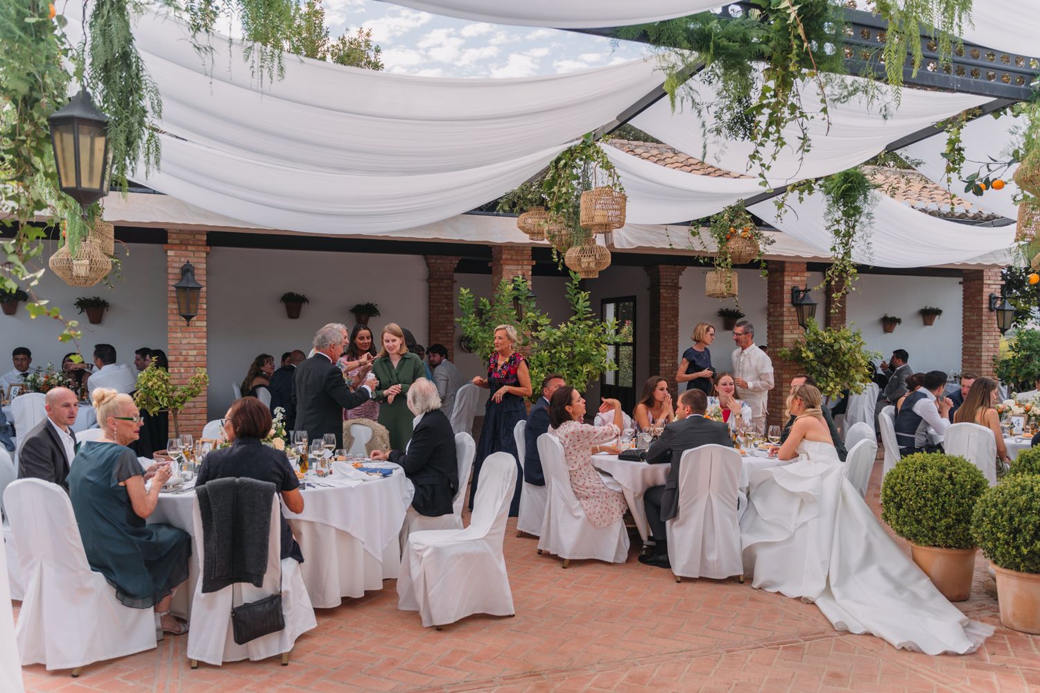 Outdoor wedding reception under draped canopies with guests seated at decorated tables.
