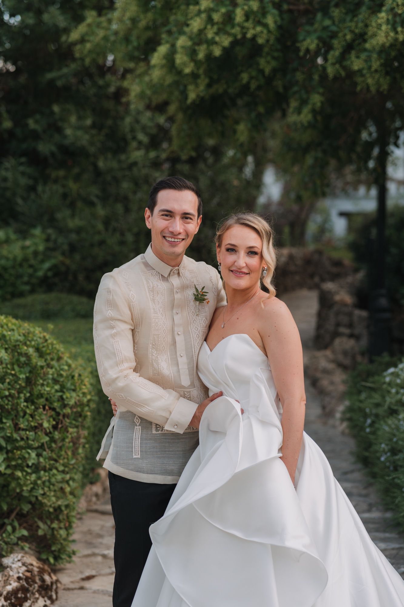 Wedding couple stands together in formal attire against a garden backdrop.