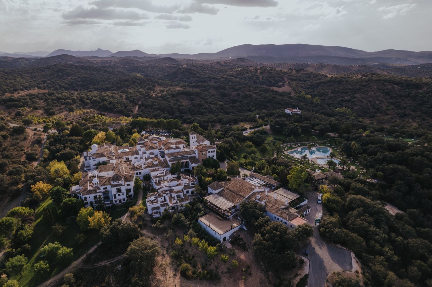 Aerial view of a charming hillside village nestled among mountains and forests during golden hour.