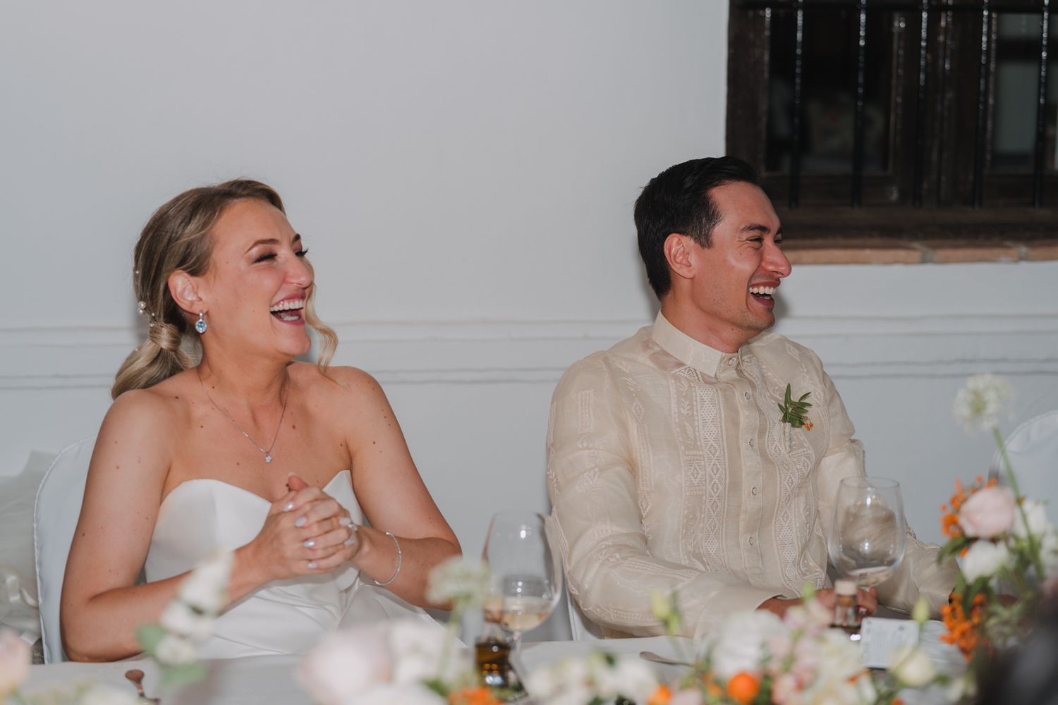 Wedding couple sharing a laugh during reception dinner with wine glasses on decorated table.