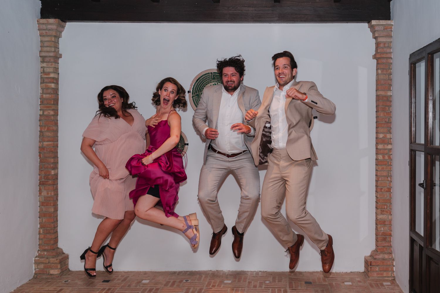 Four people jumping in the air against a white wall with brick archways.