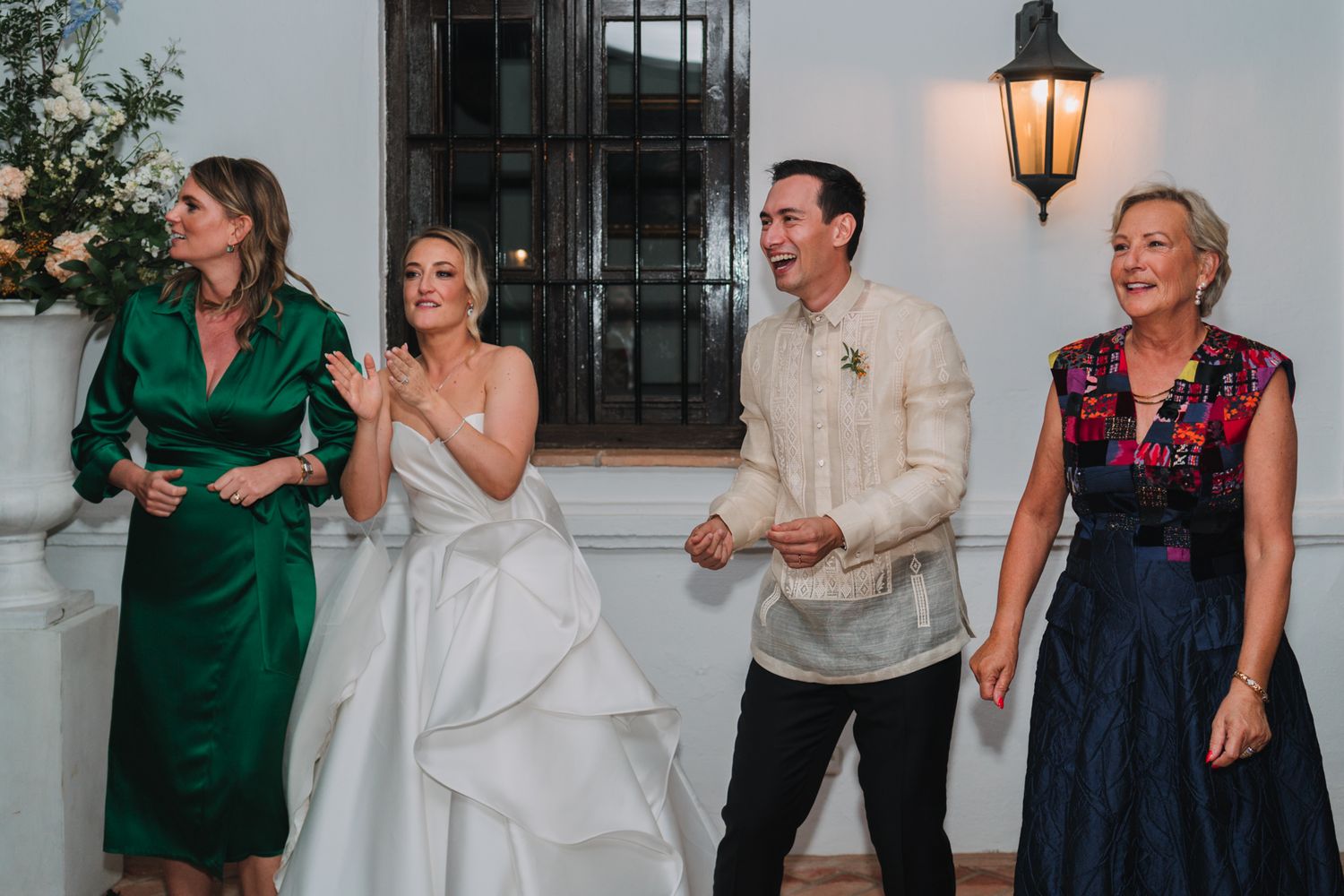 Wedding party members dancing and laughing together during a reception celebration at a venue with lantern lighting.