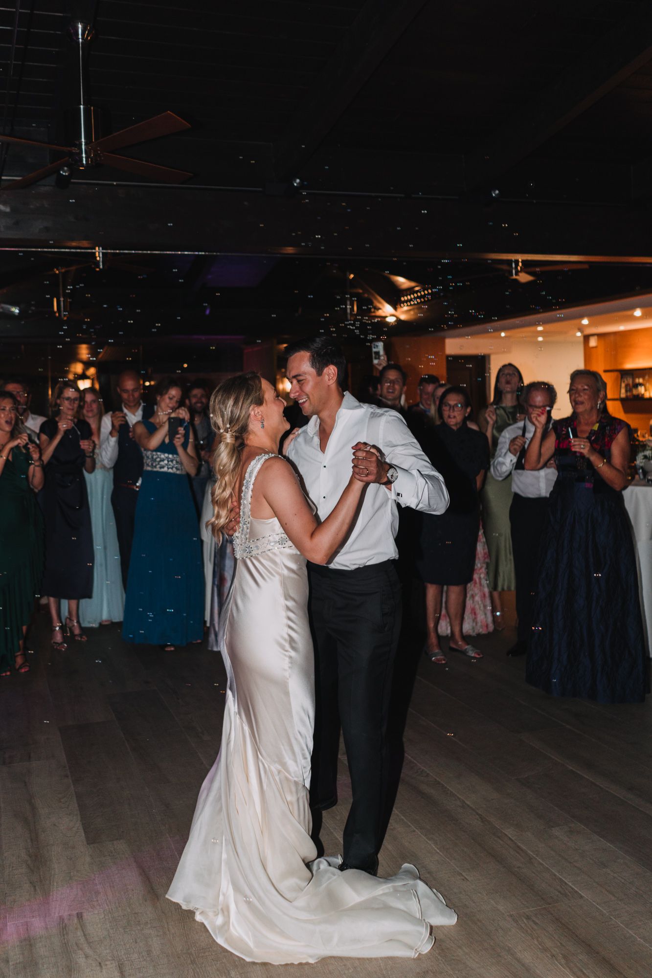 A couple shares their first dance at a wedding reception while guests watch from the dance floor.