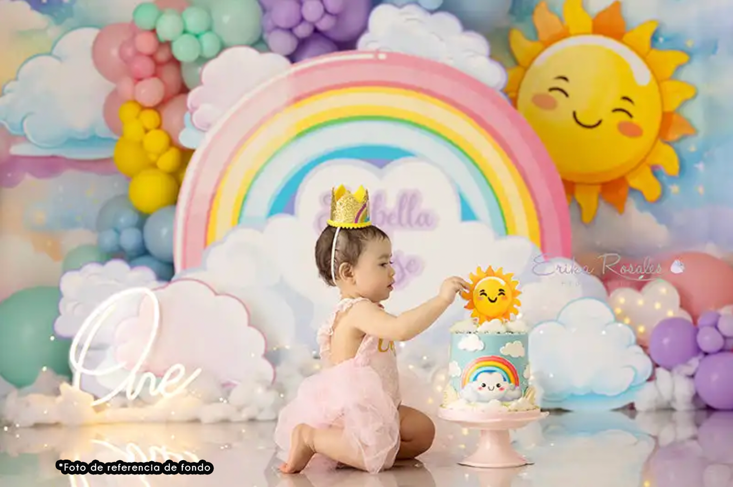 Whimsical rainbow-themed birthday setup with pastel balloon garland, smiling sun decoration and colorful cake on display.