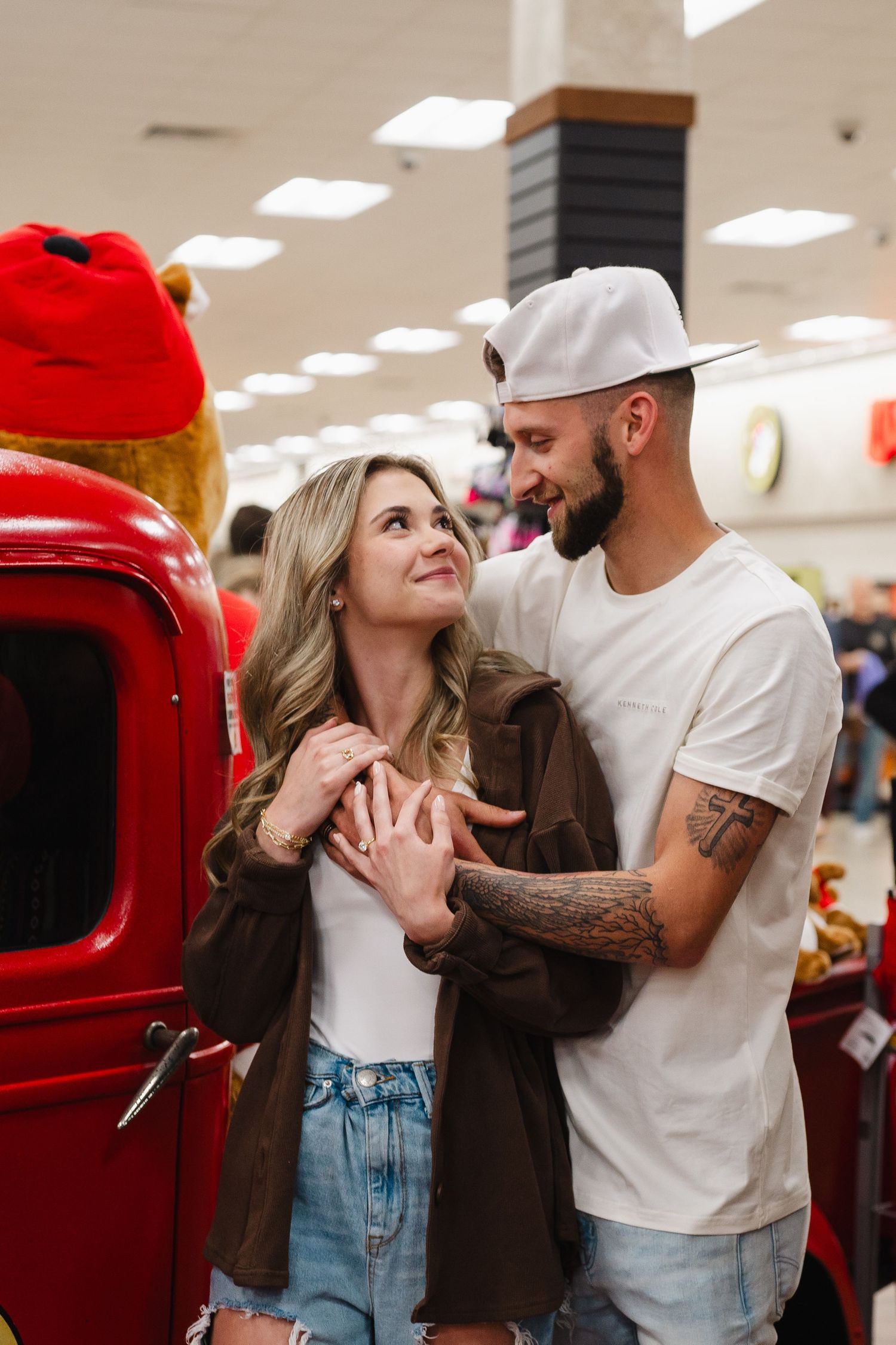 A couple shares a romantic moment while shopping, standing near a red vintage vehicle display in a retail store.