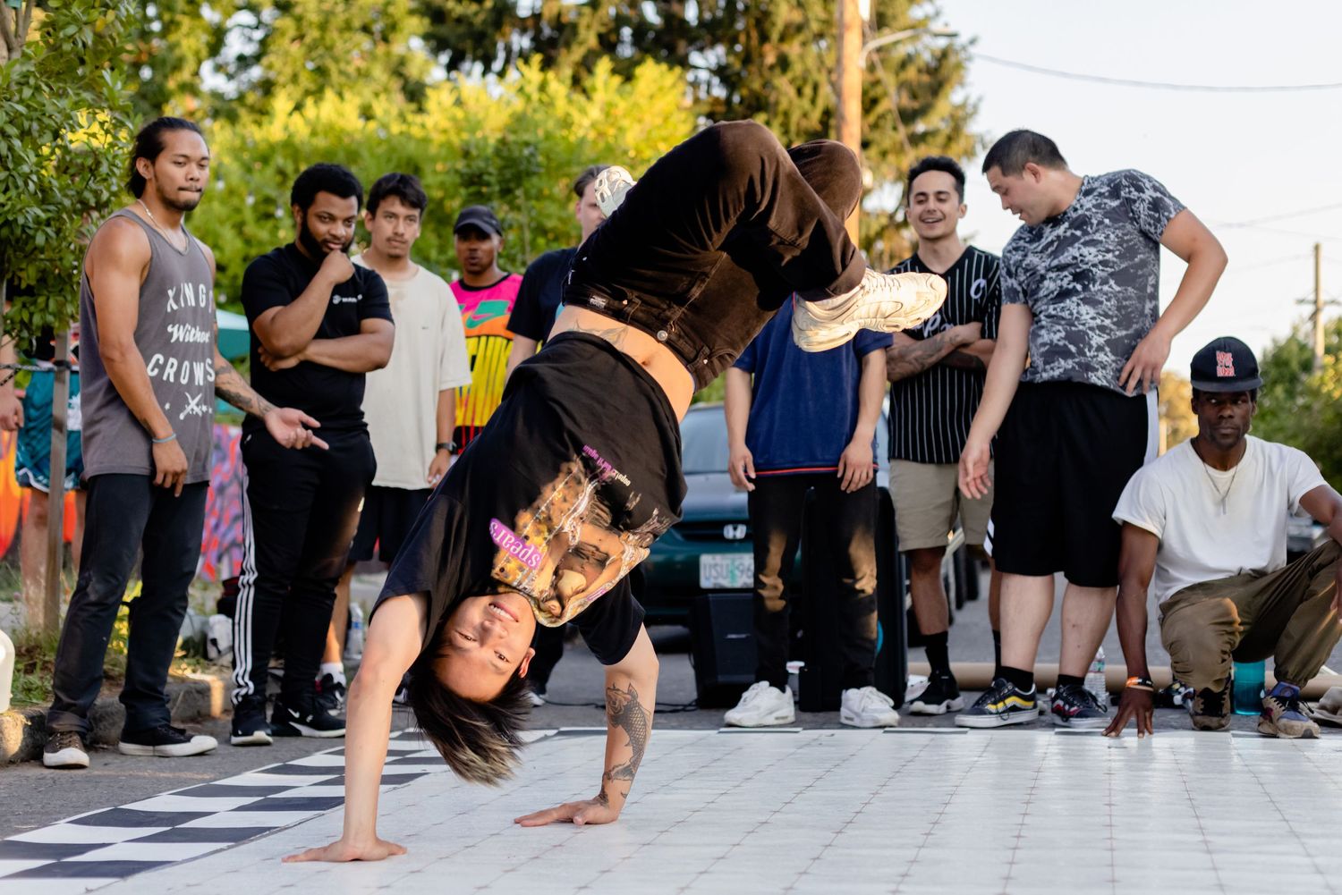 A street performer does a breakdance freeze move on a paved surface as onlookers watch in amazement.