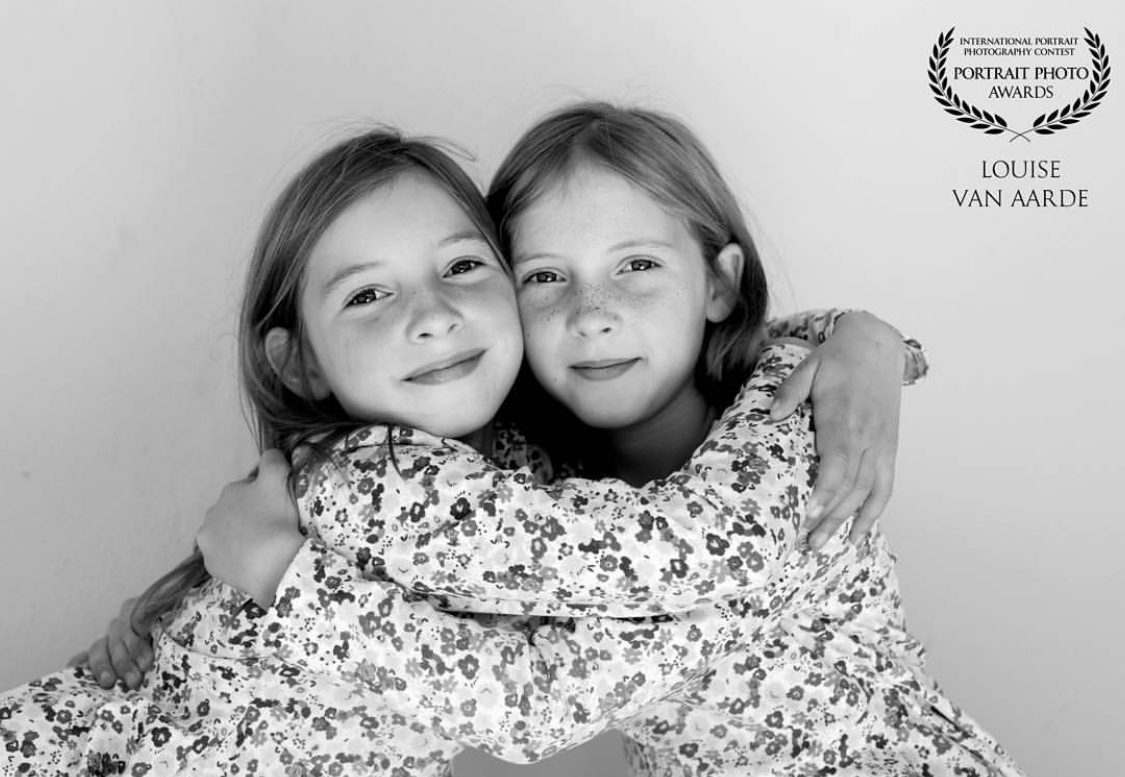 Black and white portrait of children in floral dresses hugging and smiling while laying down.