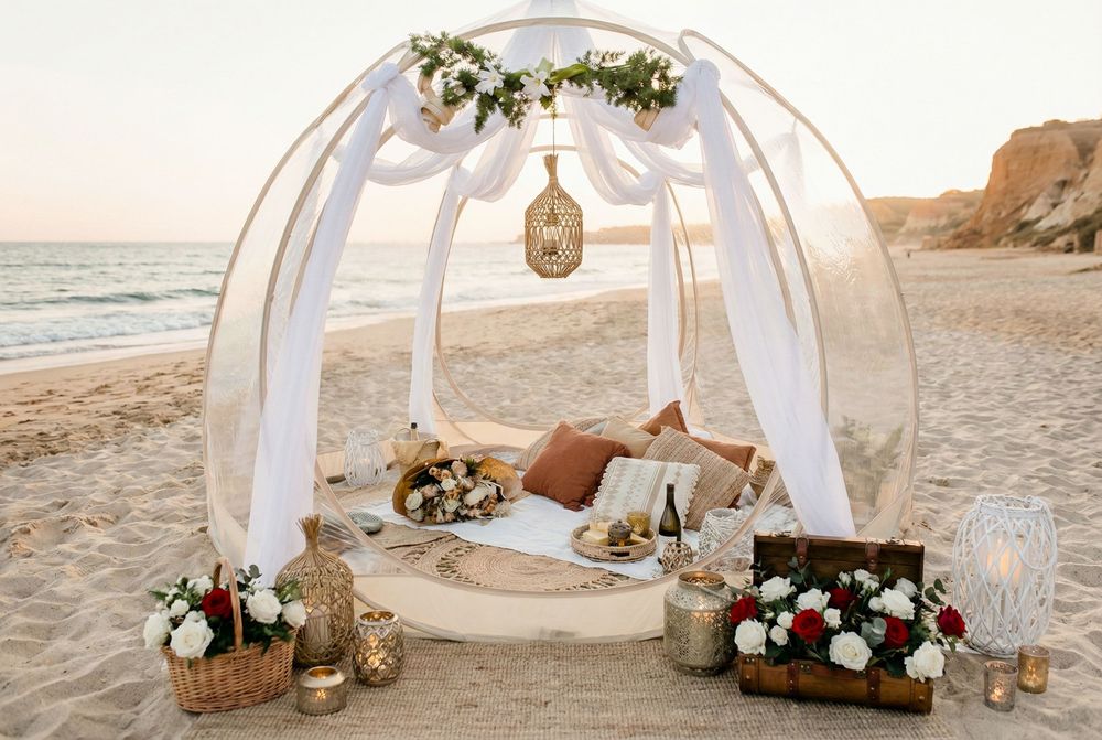 White fabric wedding arch with floral arrangements stands elegantly on a sandy beach at sunset.