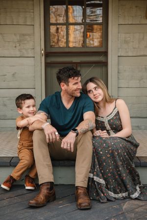 Family sitting on rustic porch steps of weathered wooden cabin.