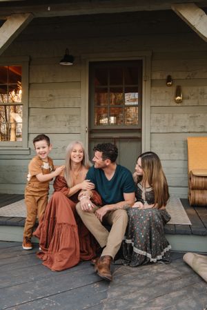 Happy family shares laughter on wooden porch of rustic cabin.
