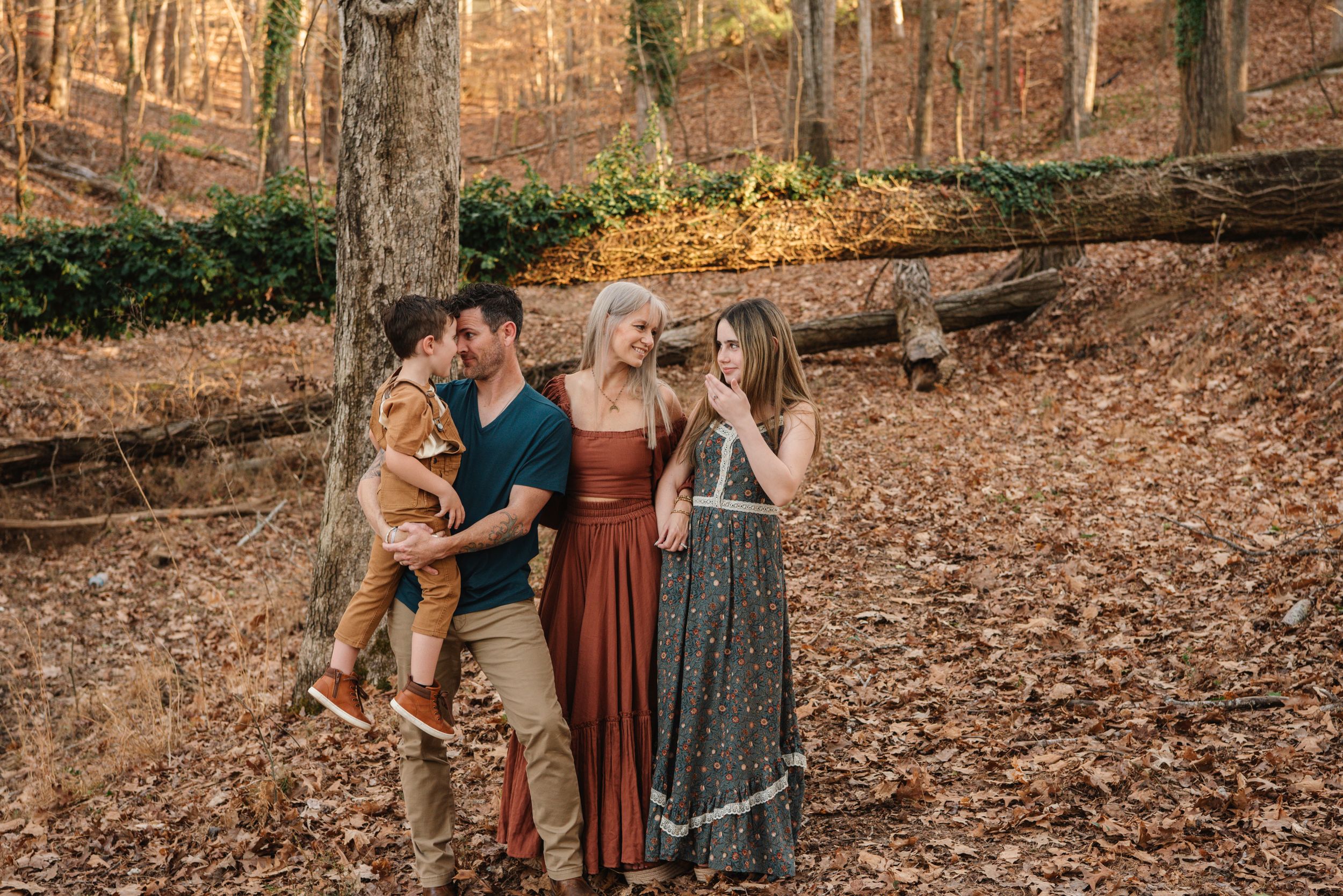 A family and their golden retriever pose together on fallen autumn leaves in a wooded forest setting.