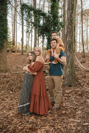 A family poses together in a wooded setting wearing coordinated earth-toned clothing.