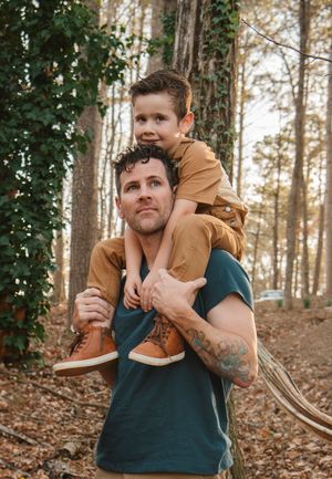 A playful piggyback ride moment captured in a wooded setting with ivy-covered trees.