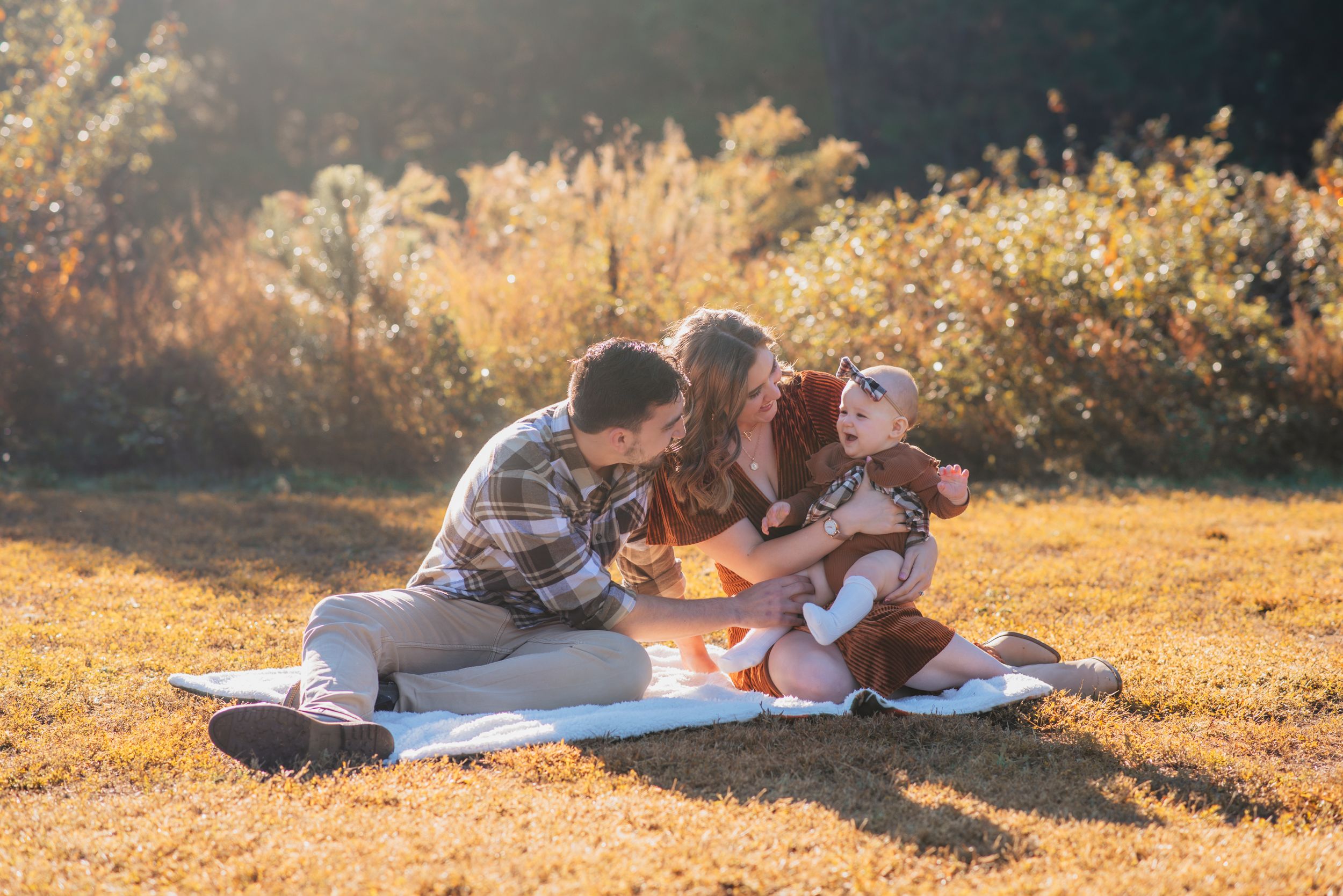 A family enjoys a picnic together on a blanket during golden hour in a sunlit field.