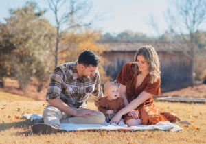 A family sits together on a white blanket during an autumn picnic with golden lighting.