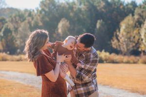 A family shares a tender moment together outdoors in autumn sunlight.
