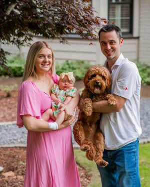 Family portrait outdoors with goldendoodle dog and baby in front of house.