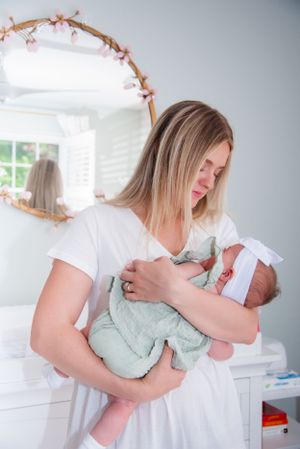 Parent in white shirt tenderly holding newborn baby in nursery with decorative mirror.