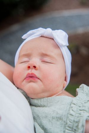 Close-up of peaceful sleeping baby wearing white bow headband and mint green outfit.