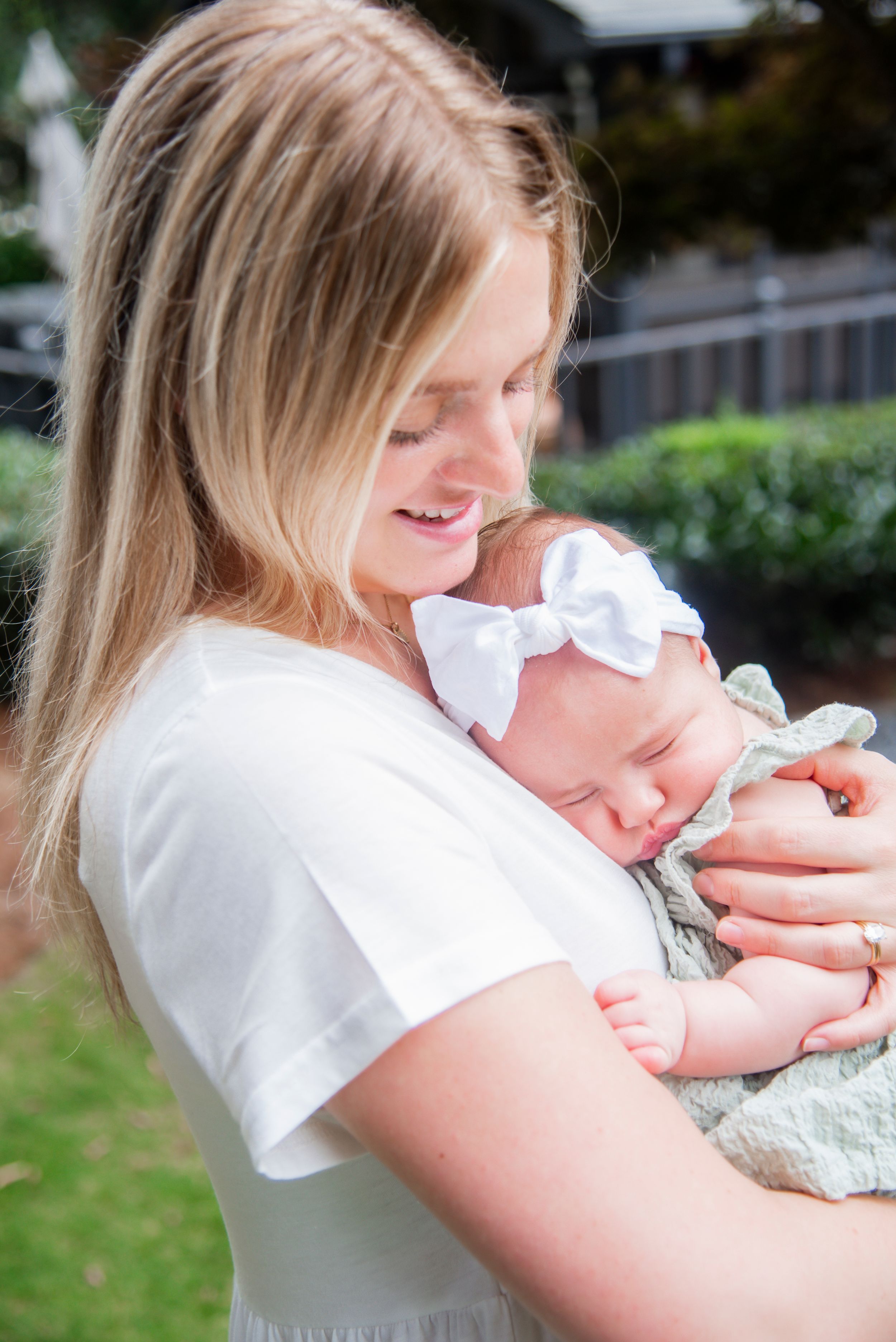 A sweet moment between parent and baby wearing a white bow outdoors in natural light.