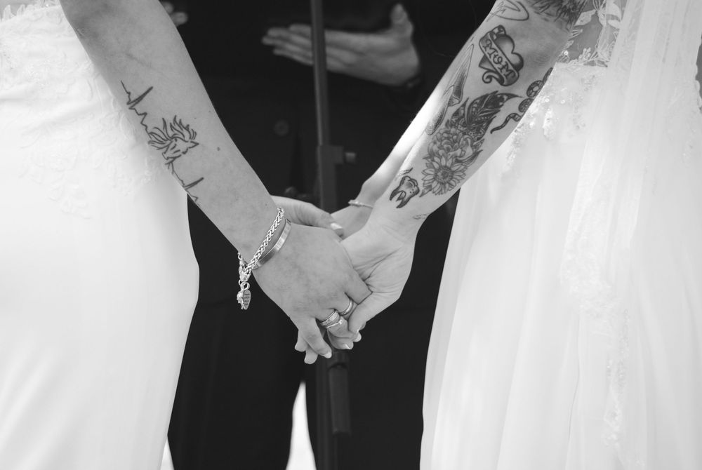 Black and white close-up of tattooed hands holding during a wedding ceremony.