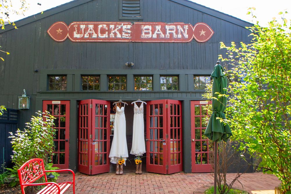 Wedding dresses hanging outside rustic red doors at Jack's Barn venue.