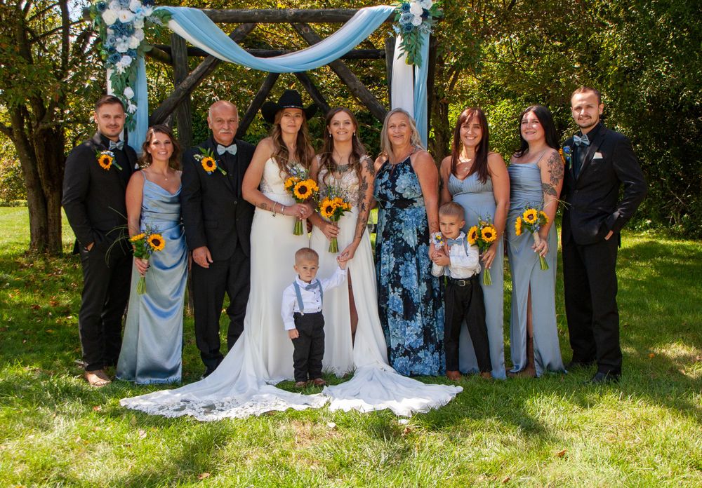 Wedding party gathered under blue archway for formal group photo in garden setting, family, wedding, brides, love