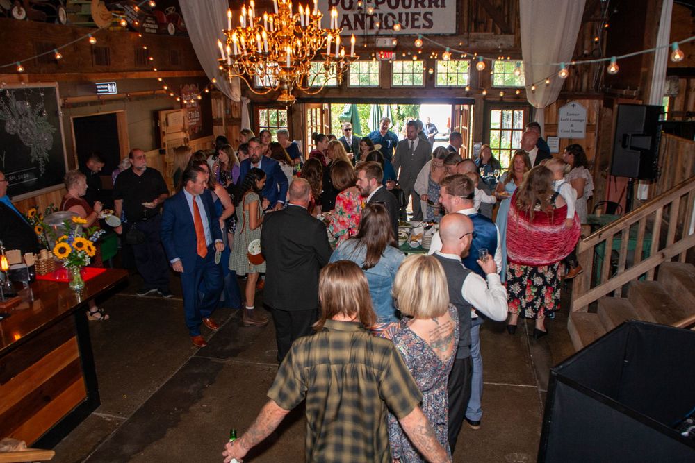 Wedding reception party guests enjoying a rustic indoor venue with chandeliers and warm lighting, dancefloor, party, reception
