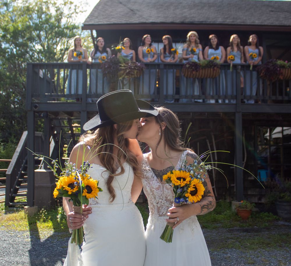 Couple sharing a romantic moment with sunflower bouquets against rustic backdrop, sunflowers, balcony, lesbians, love, wedding, bridesmaids