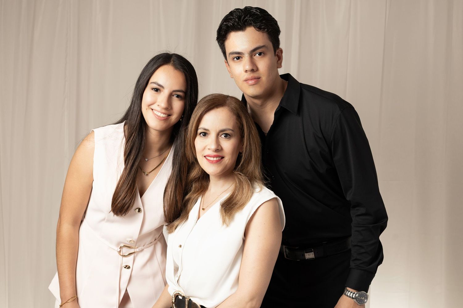 Three people posing together in a studio portrait, two women and a man dressed in smart casual attire against a neutral backdrop.