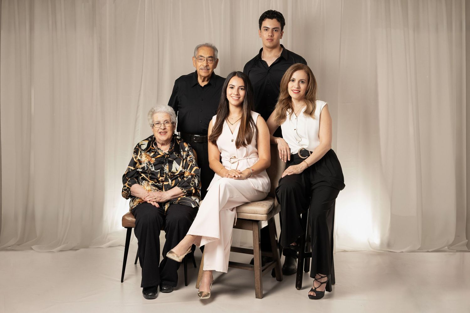 A multigenerational family of five poses together for a formal portrait against a soft white draped backdrop.