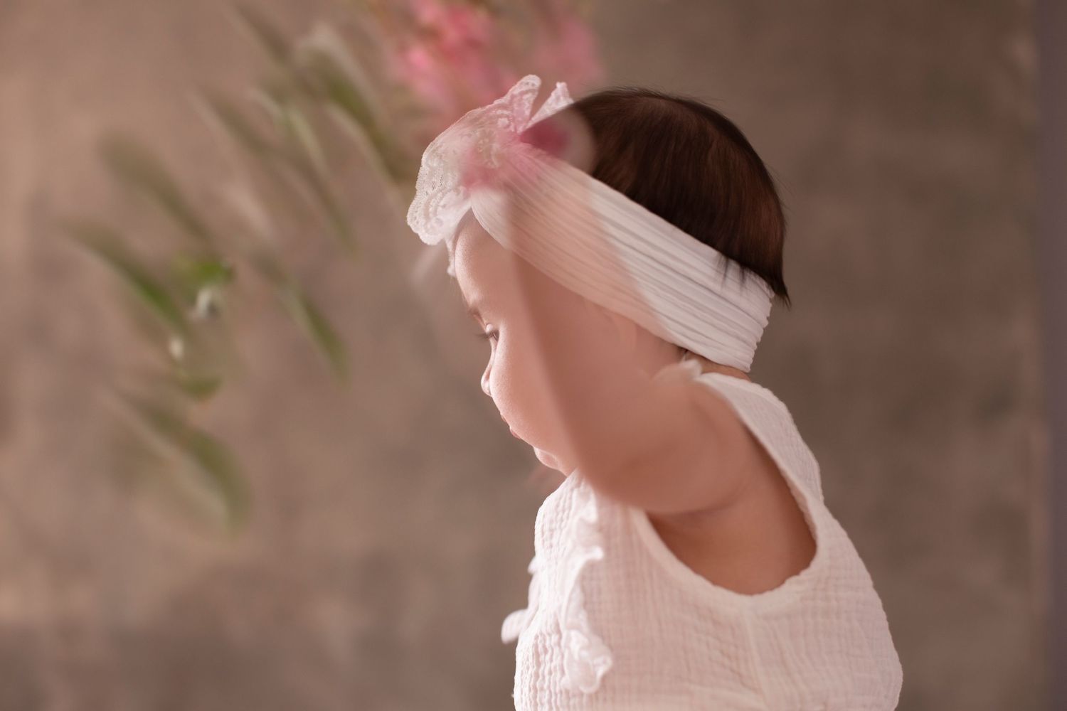 A person in white wearing a delicate mesh headband looks to the side against a textured brown background.
