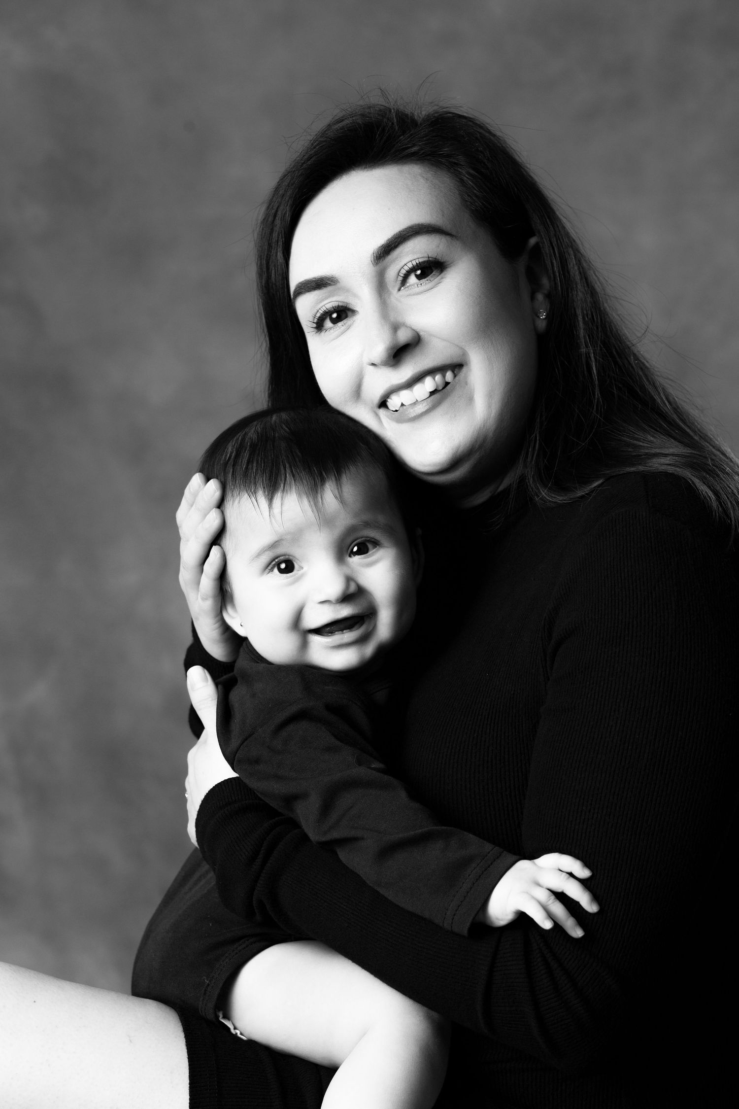 Black and white portrait of a parent and smiling baby wearing dark clothing against a mottled background.