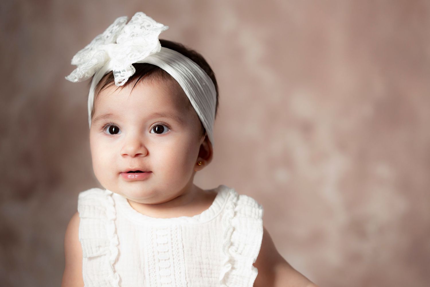 Baby wearing a white headband and dress poses for multiple professional studio portraits against a pink backdrop.