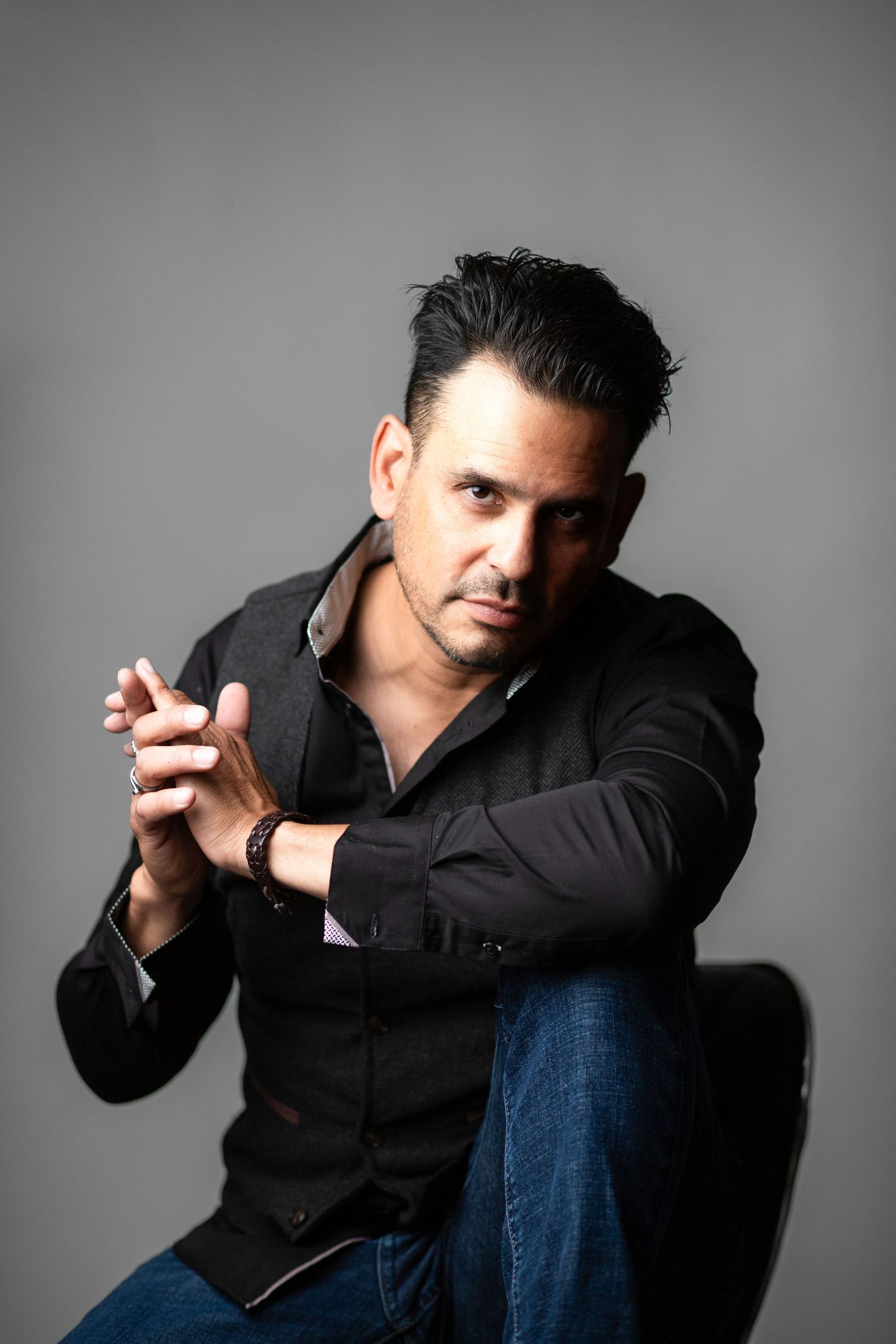 Person in black shirt and jeans poses dramatically against gray backdrop in stylized portrait sequence.