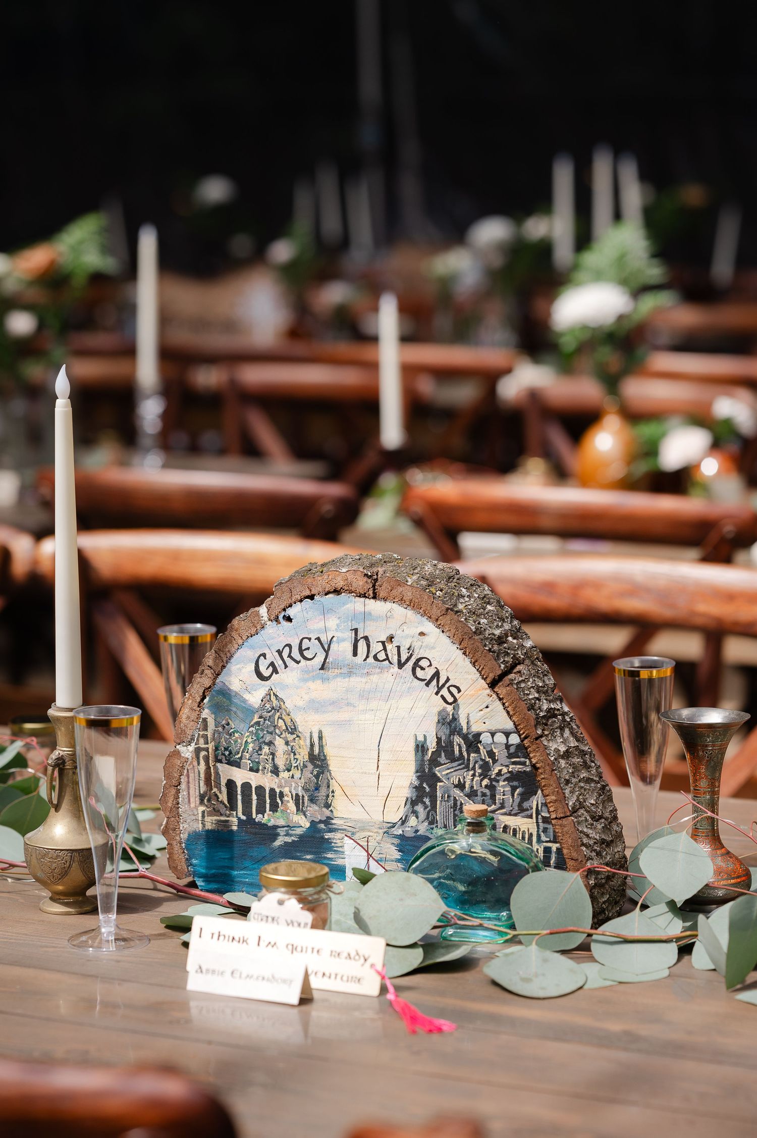 Hand-painted wooden log slice table sign reading Isengard with Orthanc tower, Lord of the Rings themed wedding decor.