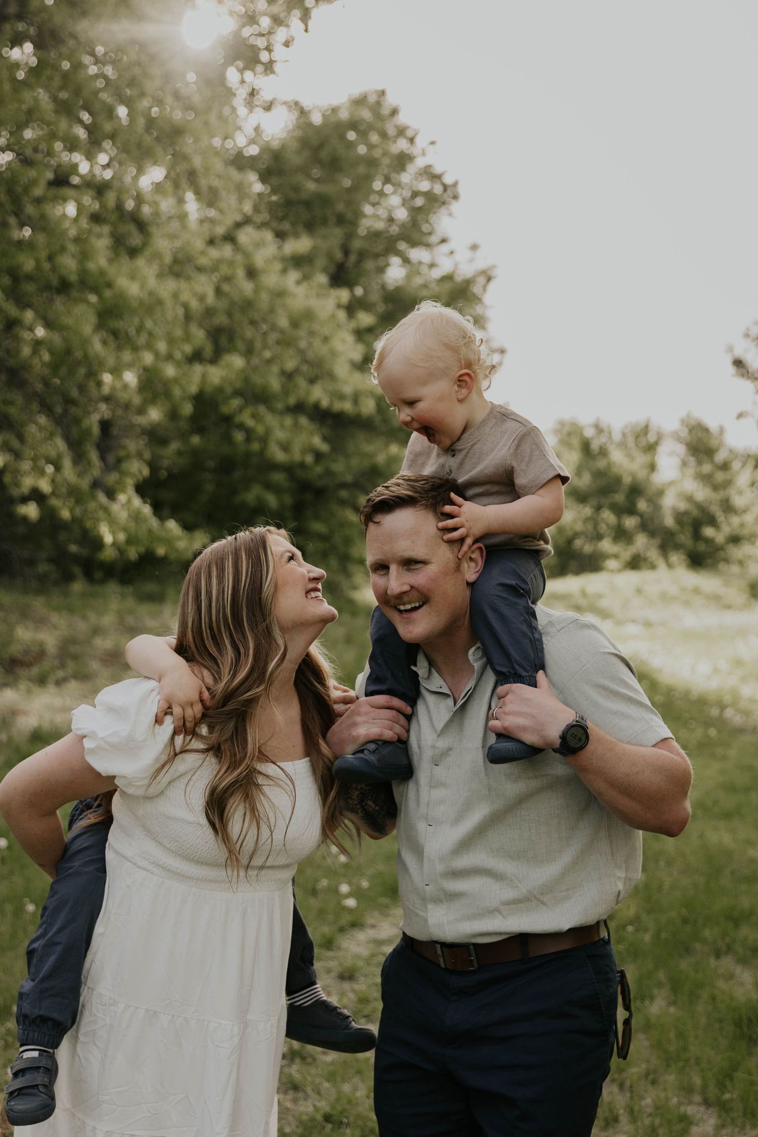 A family poses together on fallen autumn leaves beneath orange trees in a park setting during fall.