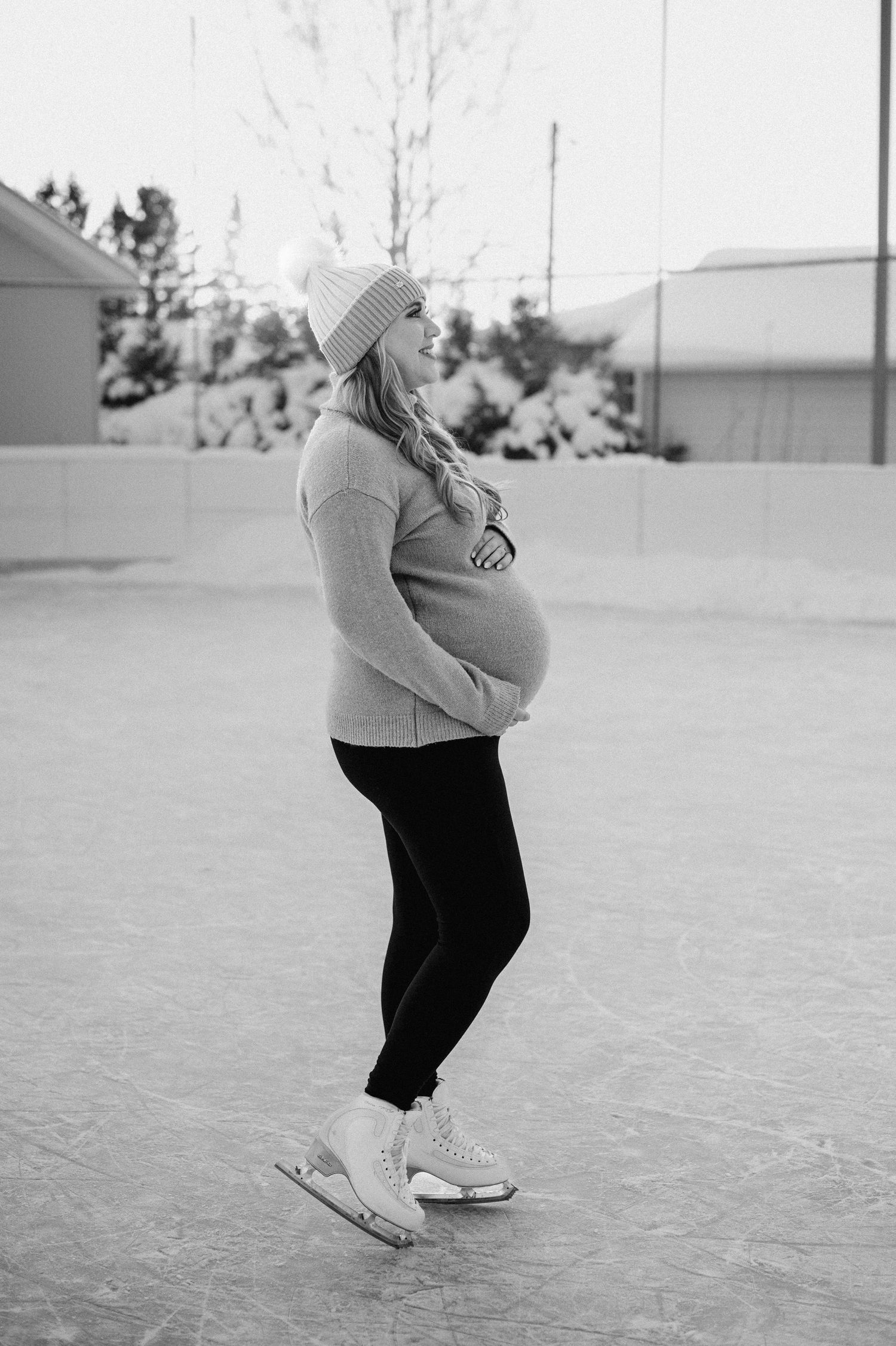Pregnant woman in winter attire poses outdoors in black and white.
