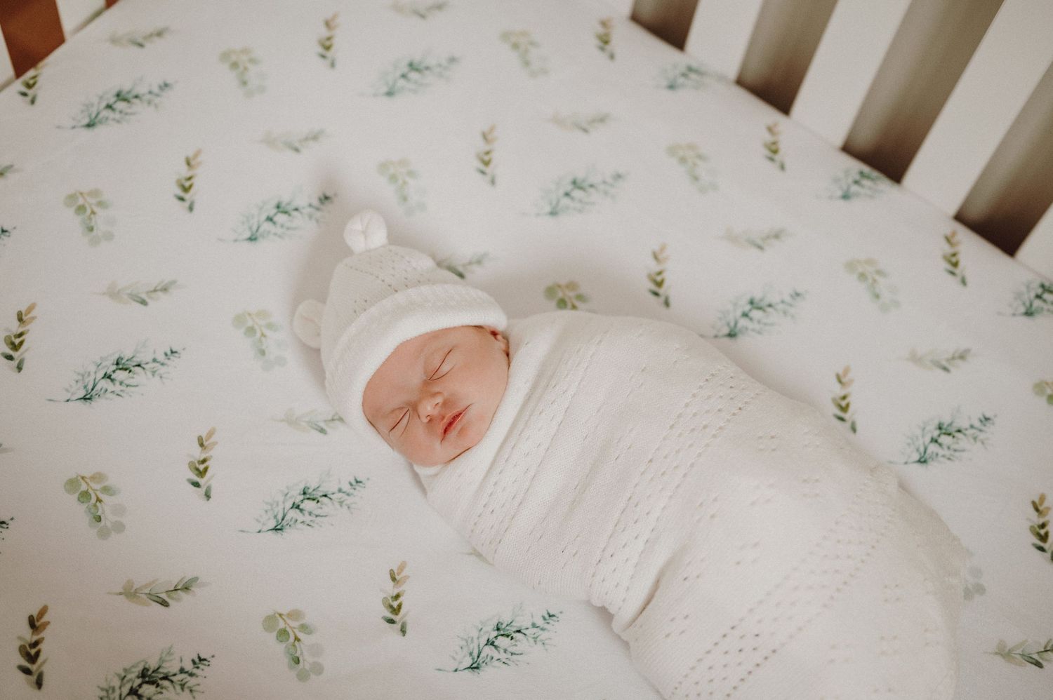Baby resting in white crib with delicate floral pattern bedding.