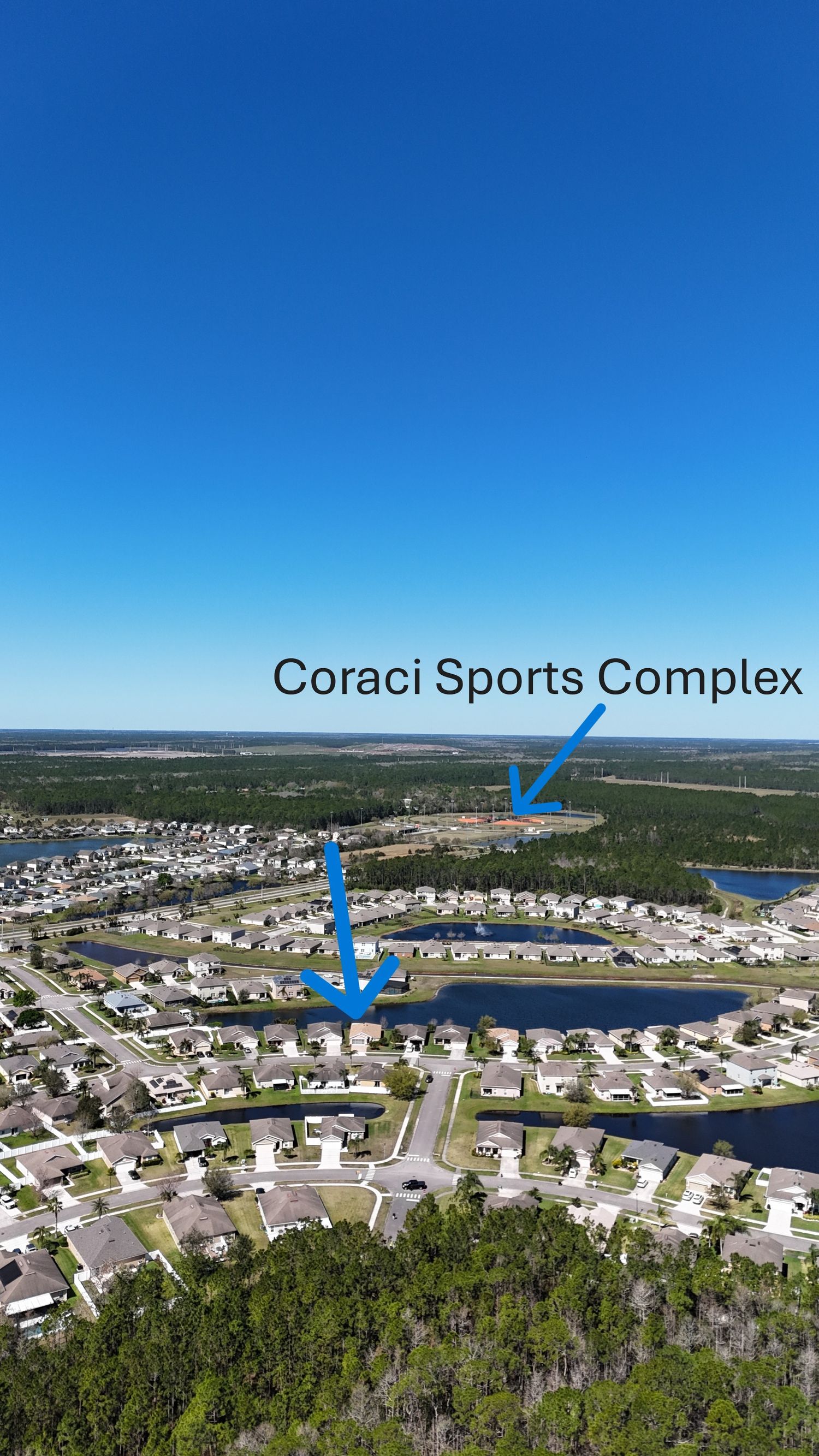 Aerial view of a waterfront residential community with the Coraci Sports Complex marked by blue arrows.