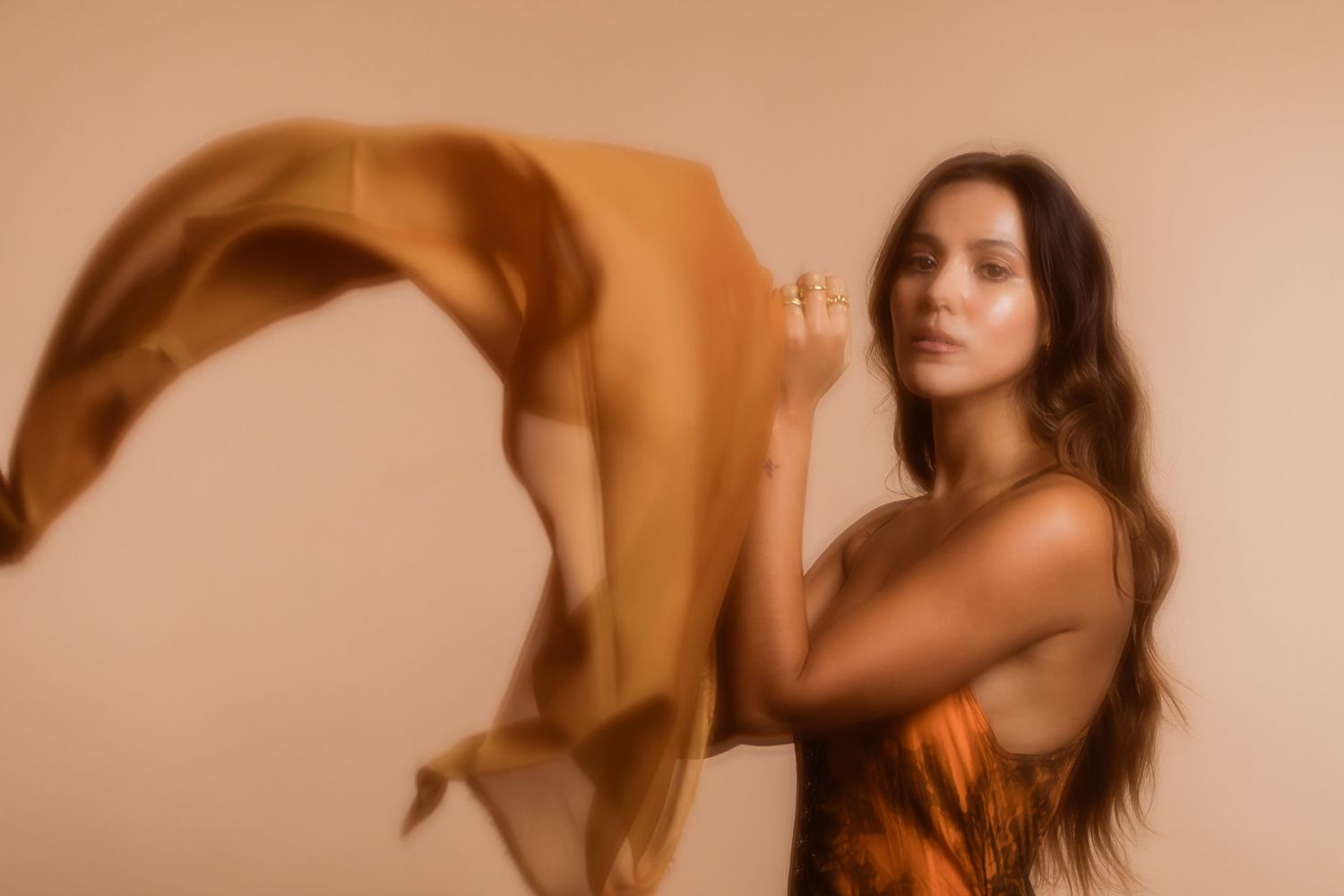 A figure in a warm-toned artistic portrait moves gracefully with flowing fabric against a sepia background.