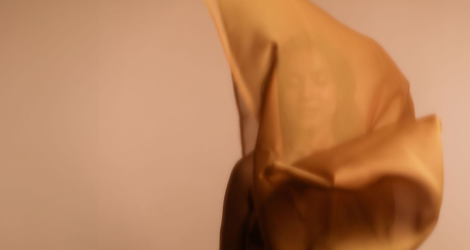 A blurred brown paper bag against a beige background creates an abstract, artistic composition.