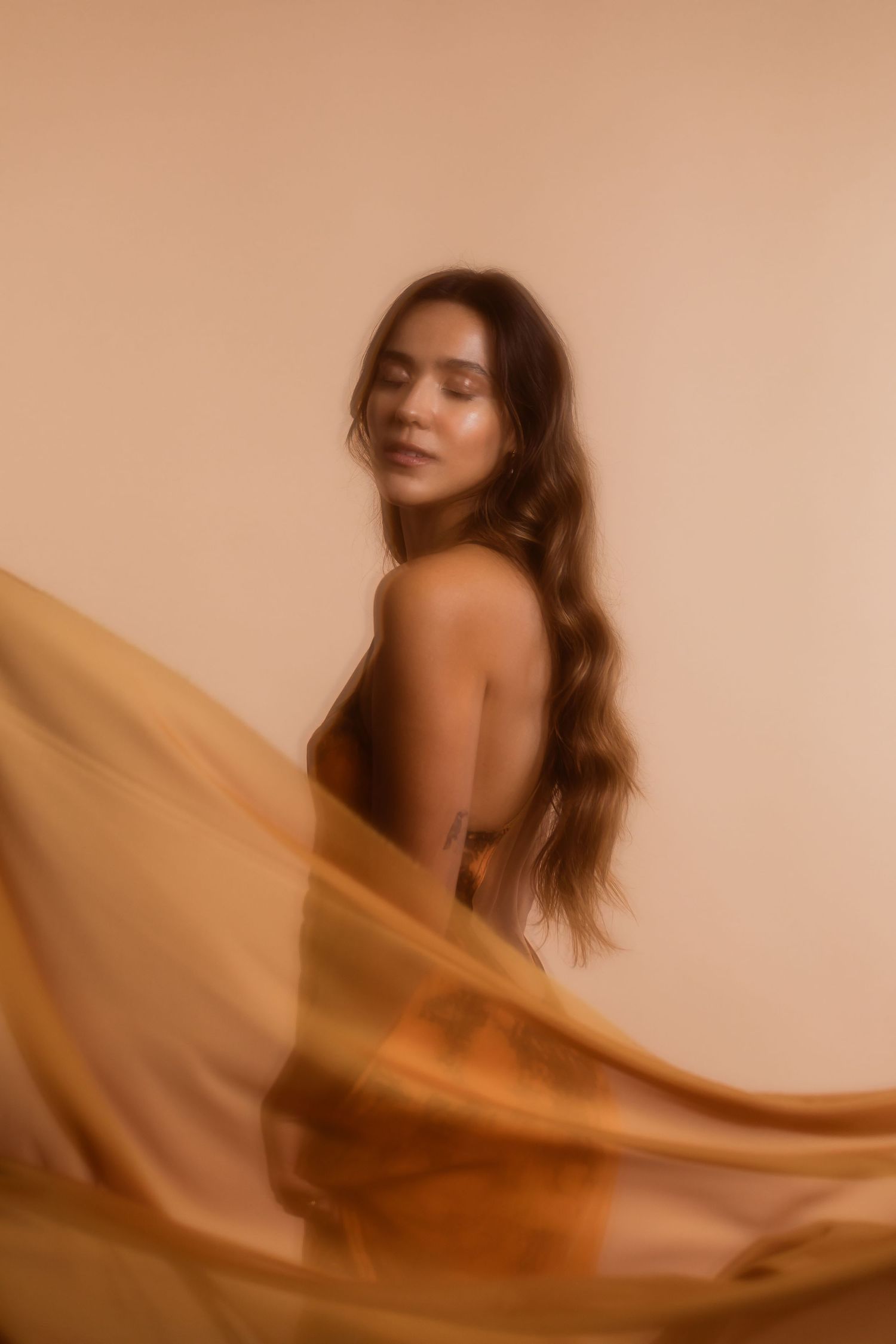 A dreamy portrait in warm sepia tones featuring long flowing hair and sheer fabric creating an ethereal mood.