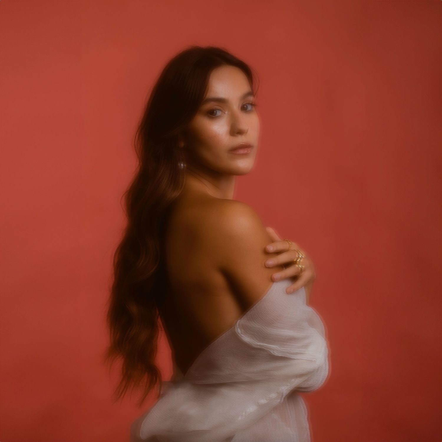 Artistic portrait with soft focus of person in white fabric against coral backdrop with long dark hair.