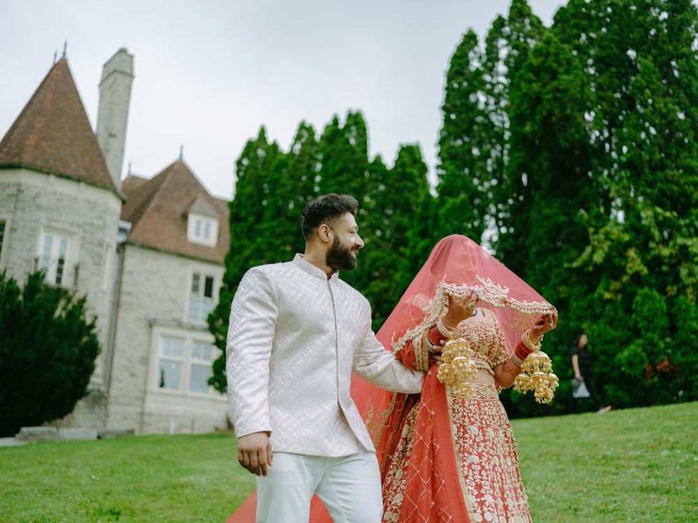 A pair in traditional wedding attire pose on castle grounds with stone towers visible behind them.