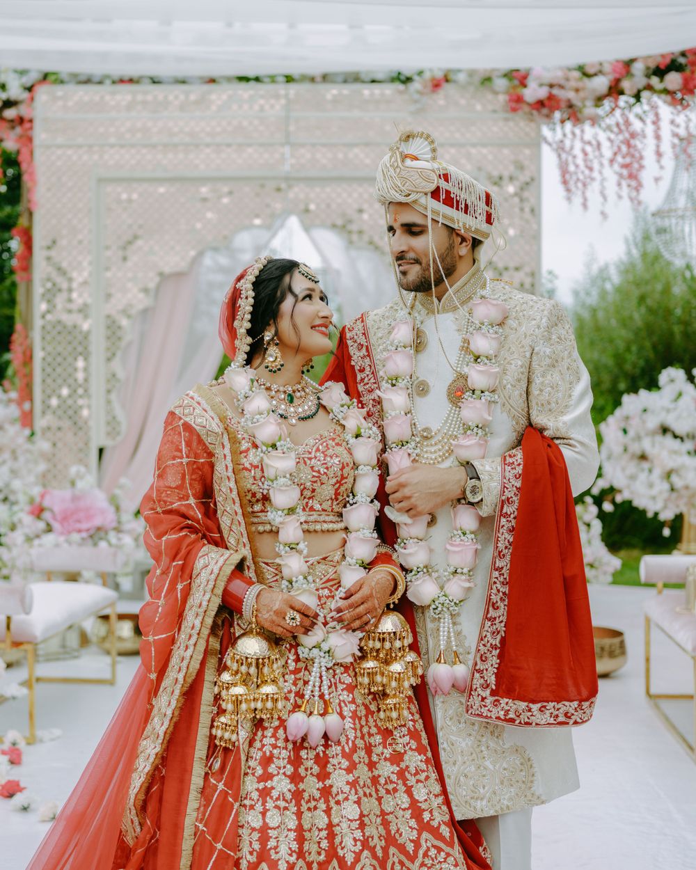 A couple in traditional Indian wedding attire share a joyful moment against a floral backdrop at their ceremony.